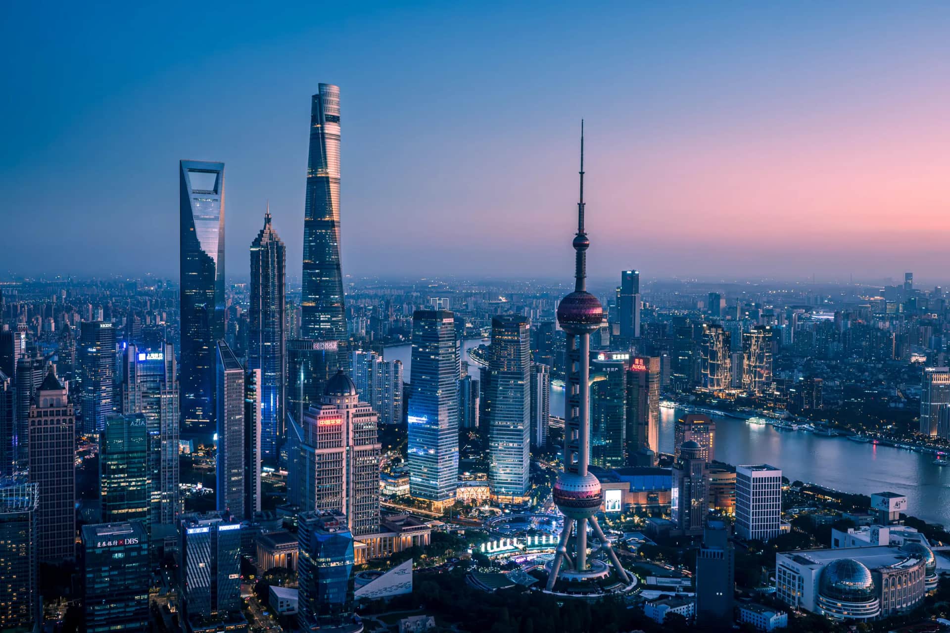 Shanghai's towers and riverfront illuminated beneath a pink evening sky